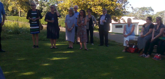 Guests stand in the shade on the edge of the green space