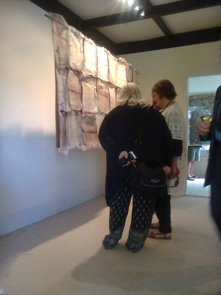 Arts journalist Rosalie Crawford in discussion. The large work is a collage of fibre, paper and assorted materials with each page covered in cursive written text.